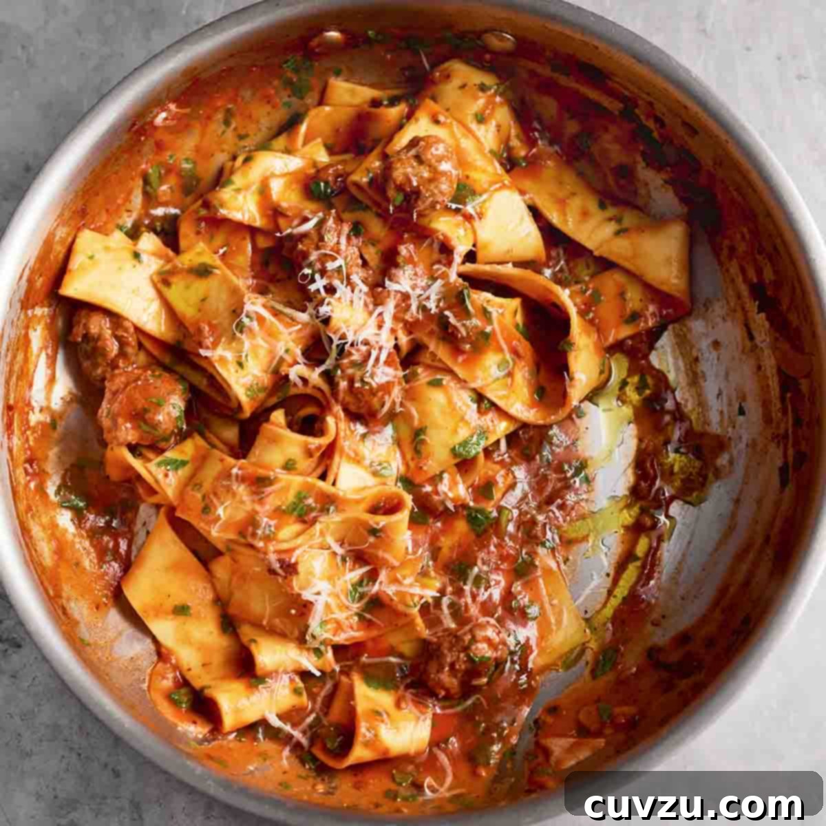 A metal skillet filled with sausage pappardelle with grated Parmesan on top.