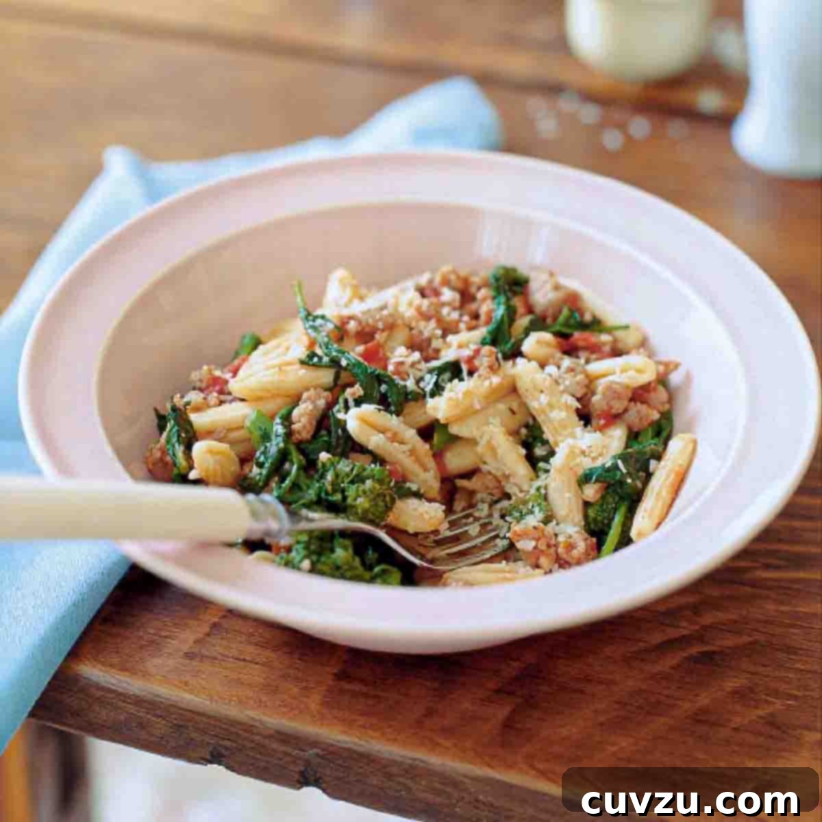 Bowl of cavatelli with turkey sausage, tomato, and broccoli rabe on a table, with a spoon.