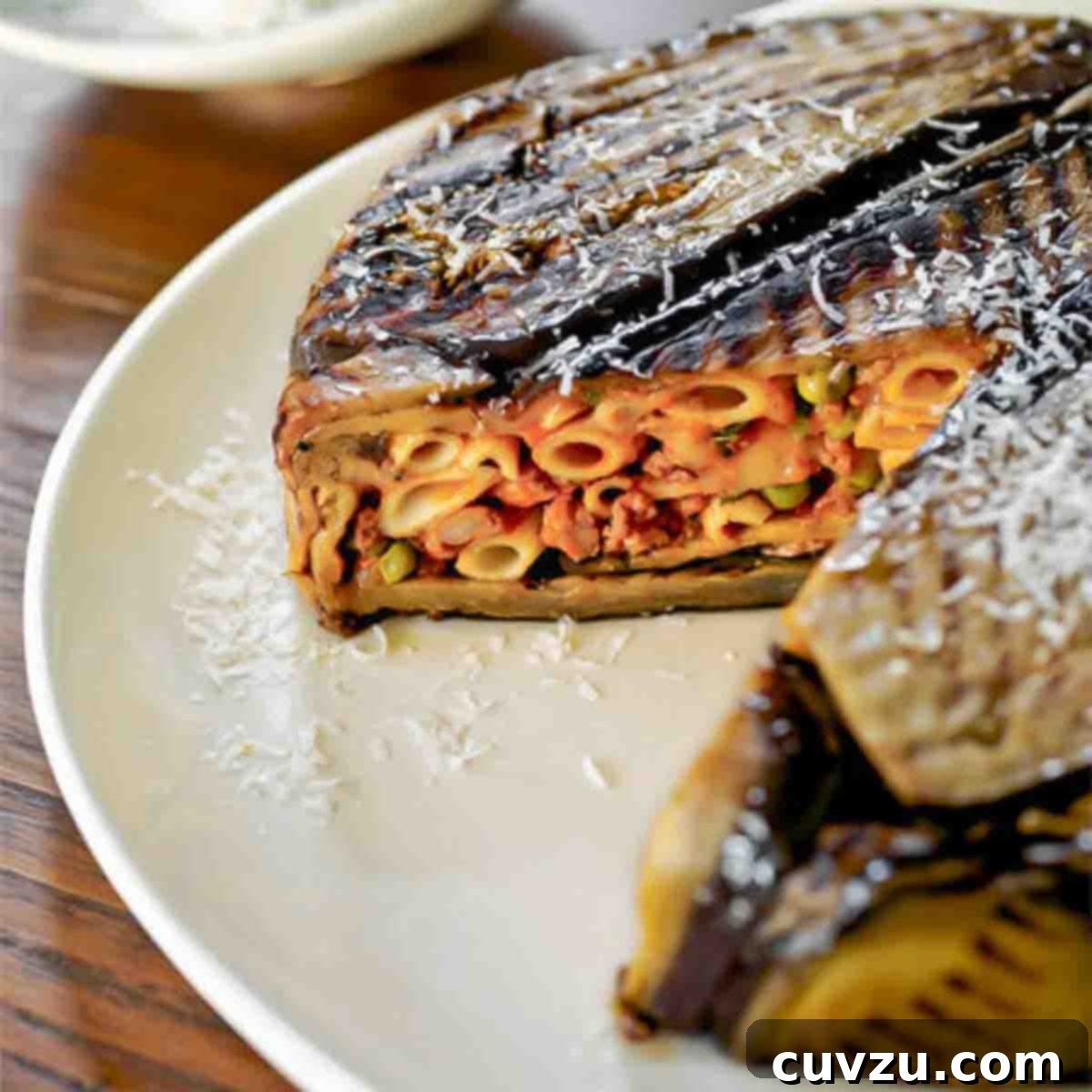 An eggplant timbale with one wedge cut from it on a white plate.