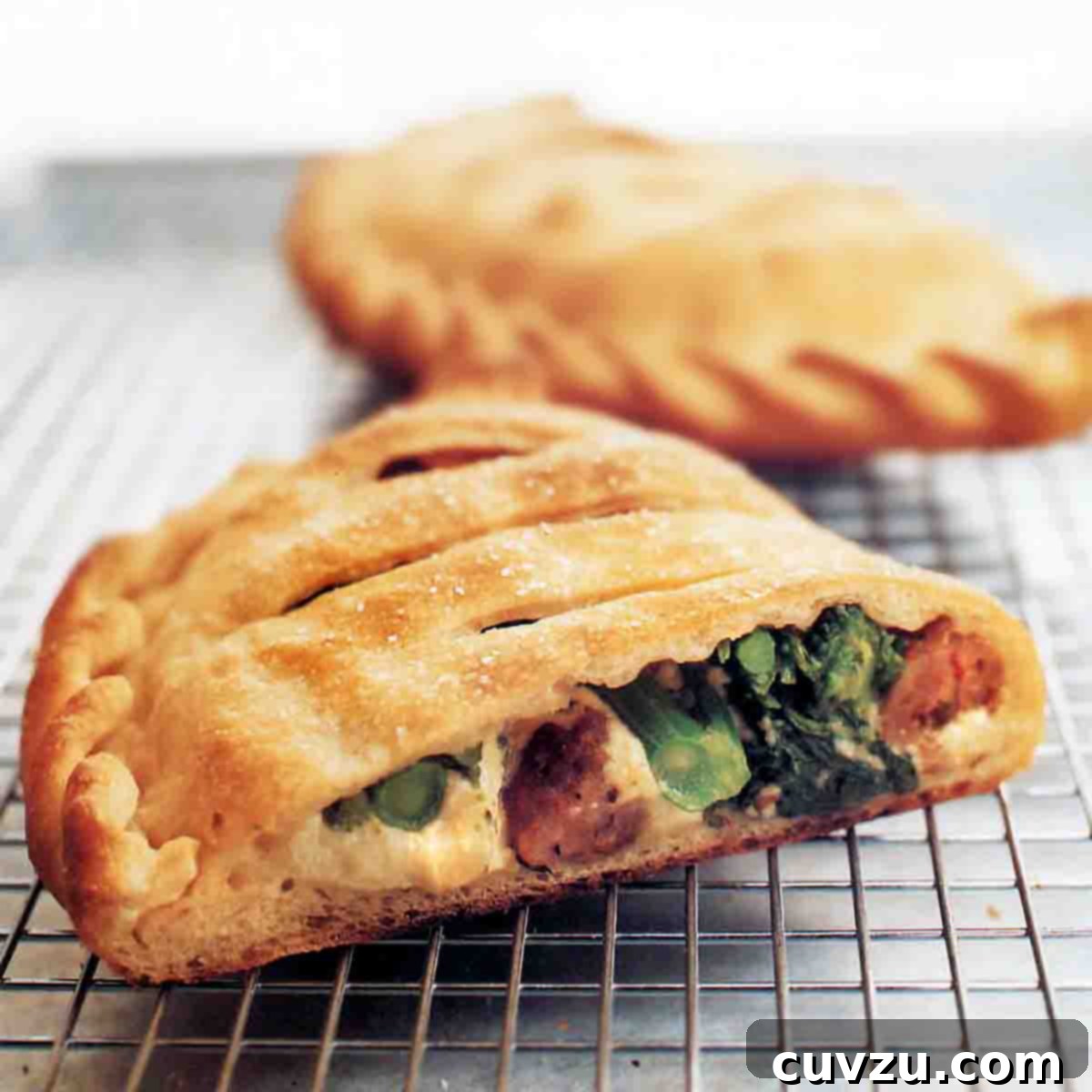 Two ricotta calzones with sausage and broccoli rabe, one cut in half, the other whole, on a wire rack.