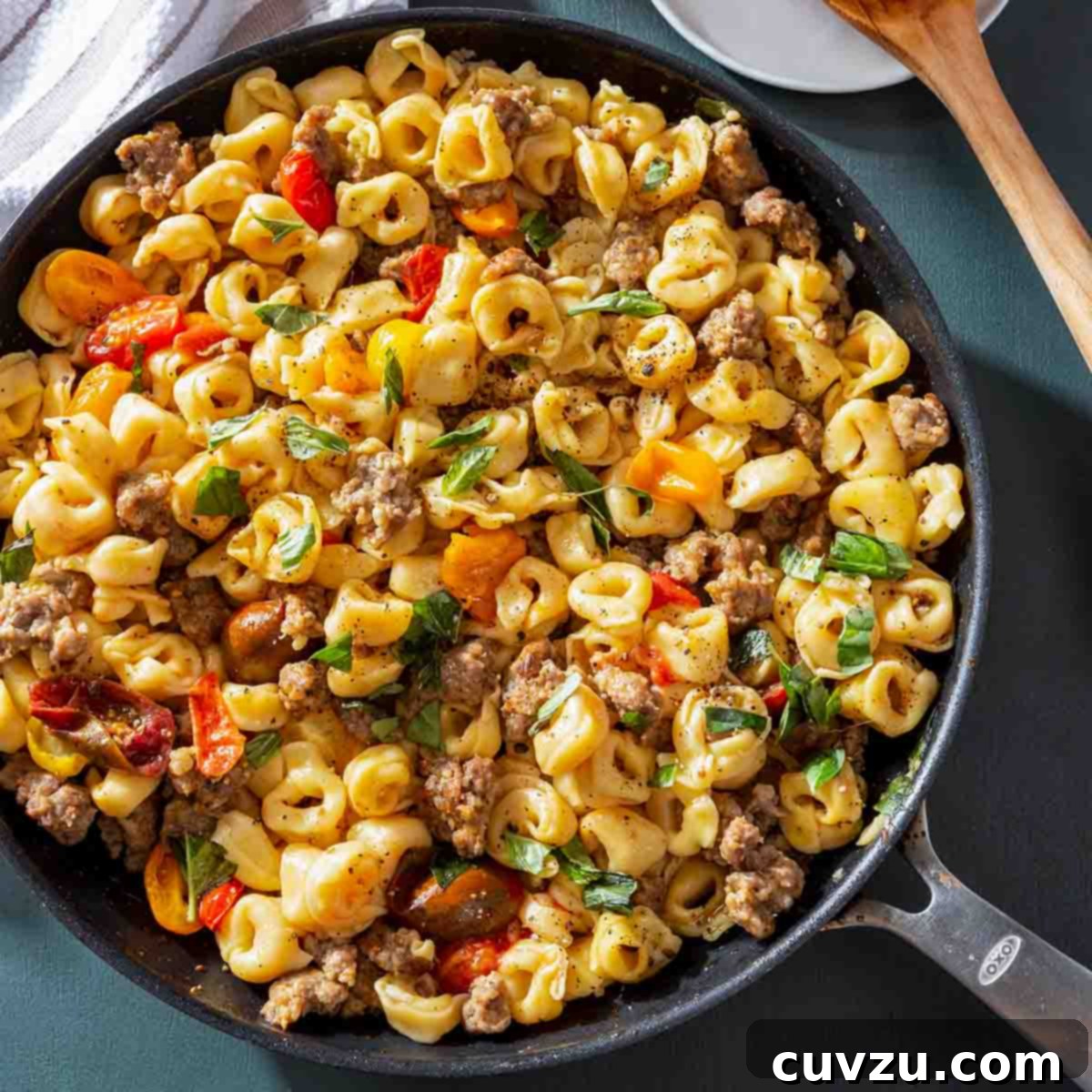 A pan of skillet tortellini with sausage and cherry tomatoes sprinkled with chopped basil.