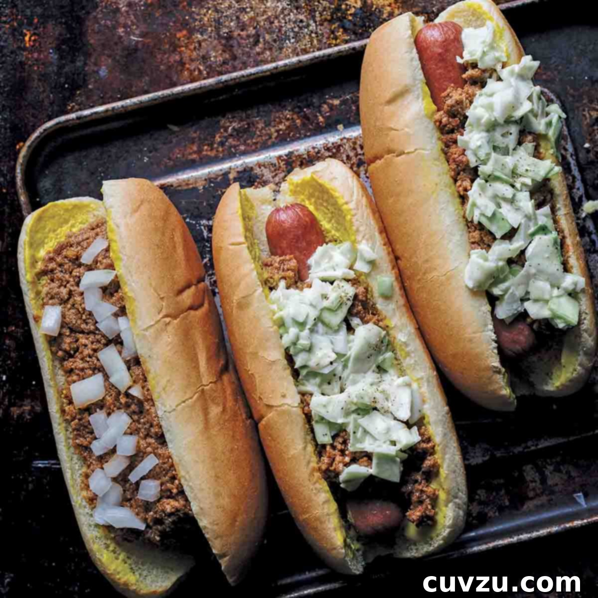 One chili bun and two slaw dogs on a rimmed baking sheet.