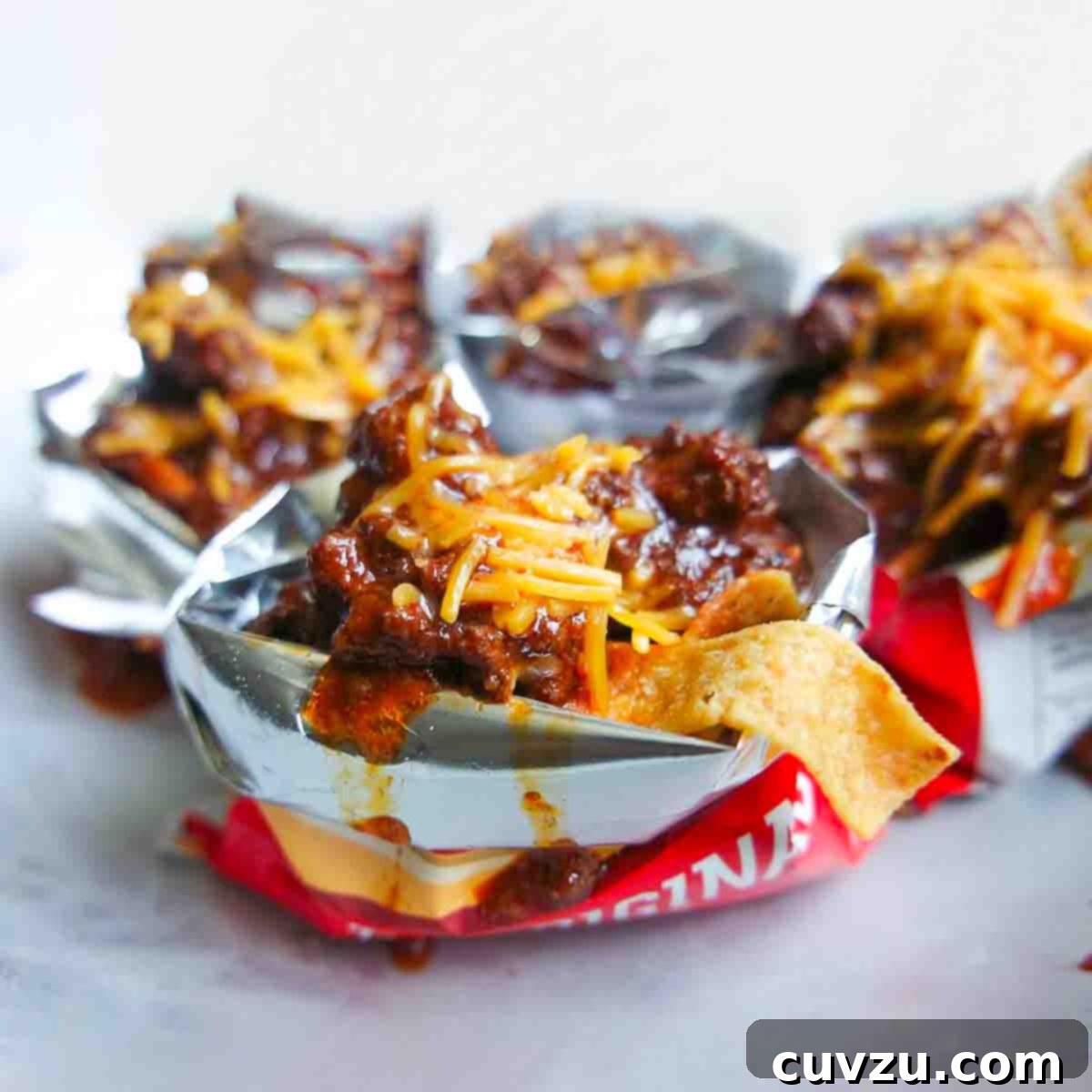 Chili and grated cheddar on top of Fritos in open mini bags of Fritos.