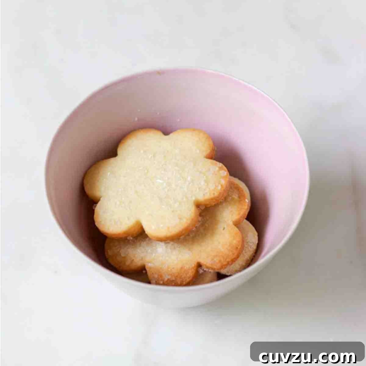 A pink bowl filled with flower-shaped sugar cookies topped with decorating sugar.