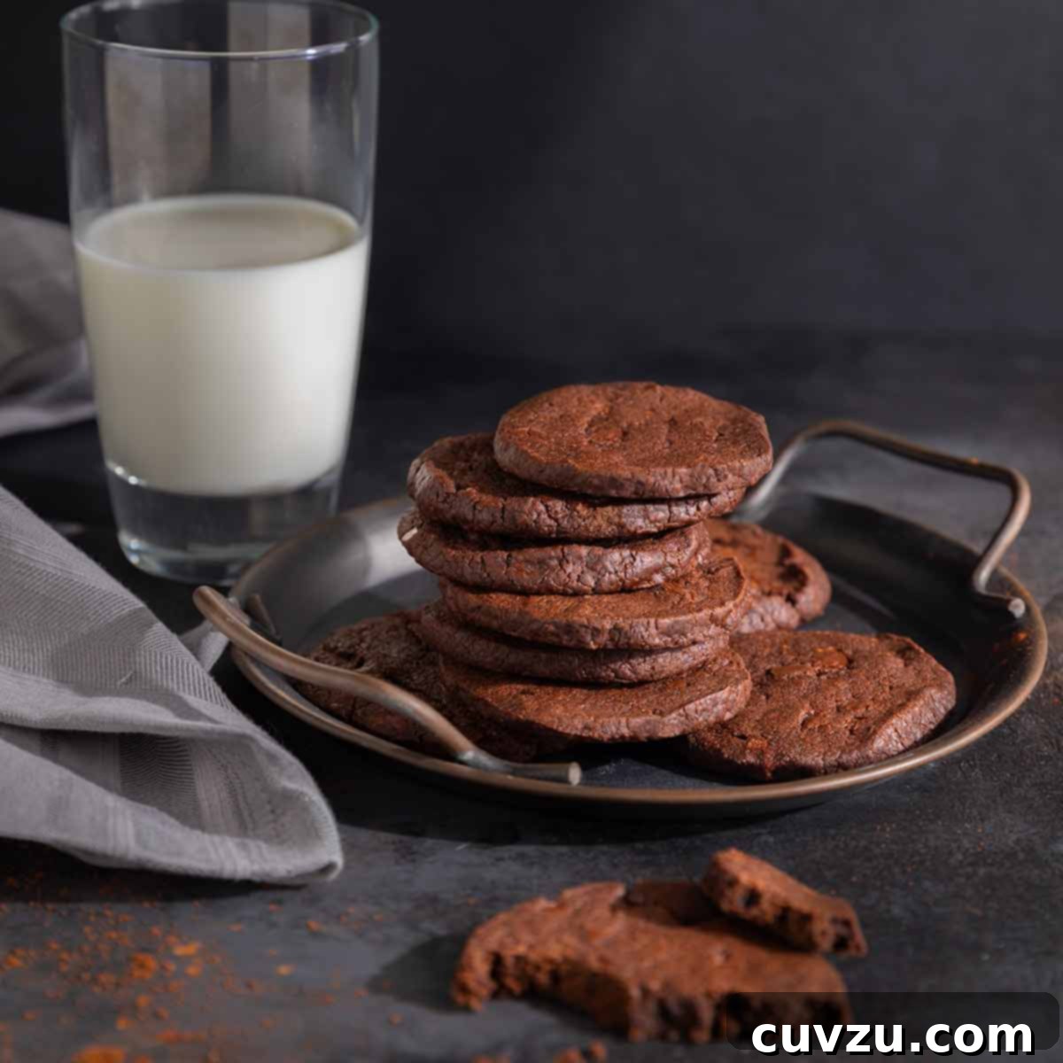 A metal tray with a pile of chocolate espresso shortbread cookies on it. Nearby, a glass of milk.