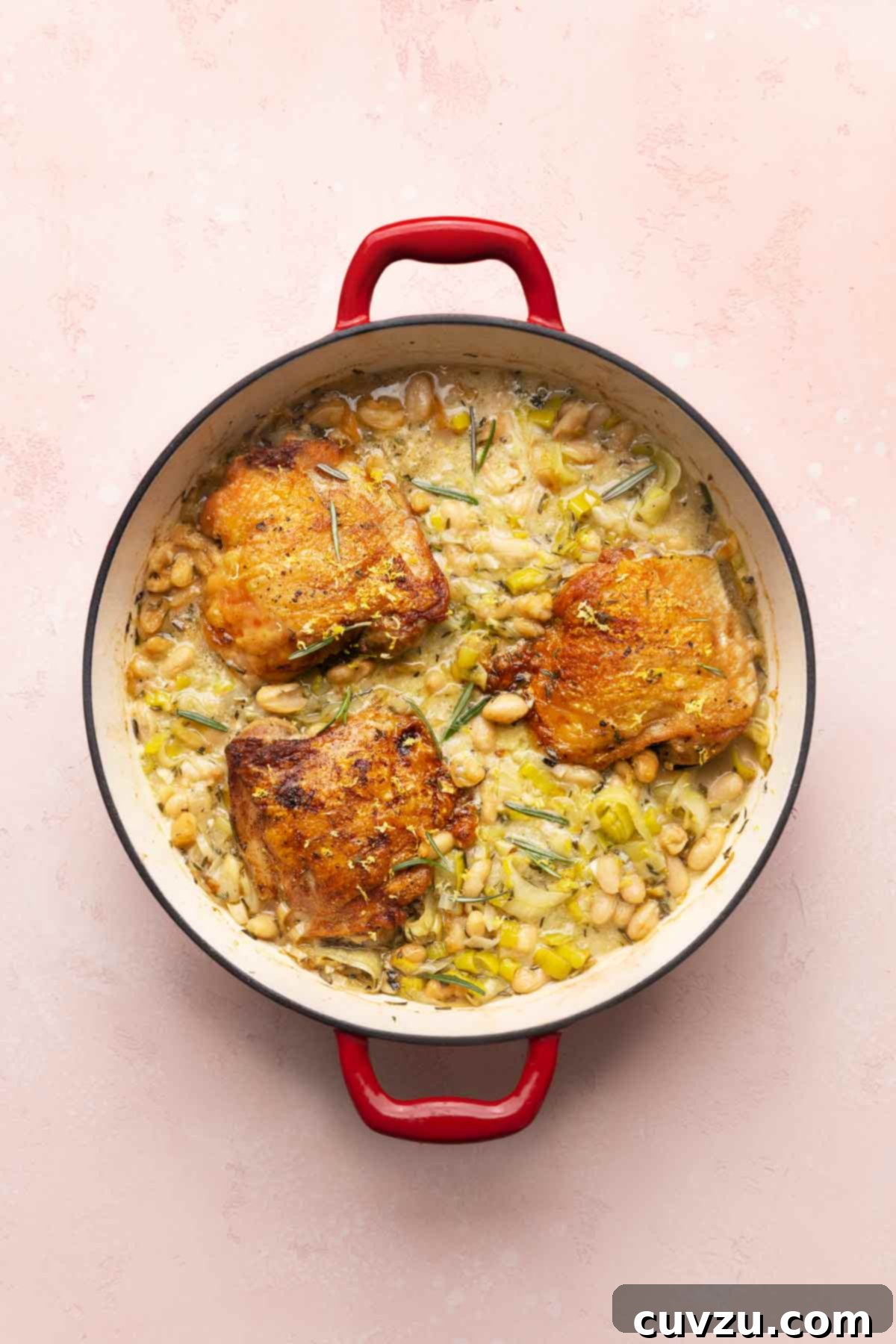 Velvety Cider-Braised Rosemary Chicken with Cannellini Beans 10 A deep skillet filled with three golden-brown rosemary chicken thighs, nestled on a vibrant bed of leeks and creamy cannellini beans, reflecting the comforting essence of a perfect one-pot meal.