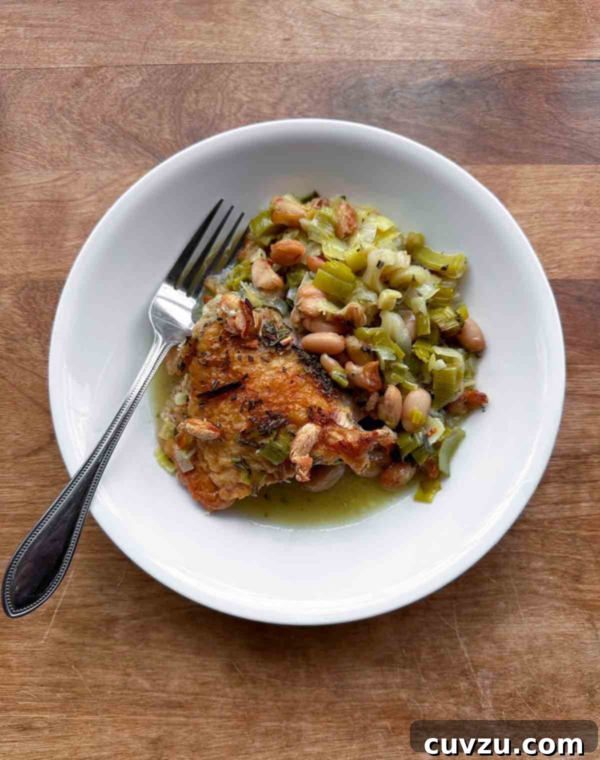 Velvety Cider-Braised Rosemary Chicken with Cannellini Beans 22 A perfectly cooked piece of rosemary chicken served with tender butter beans and soft leeks on a elegant white plate.