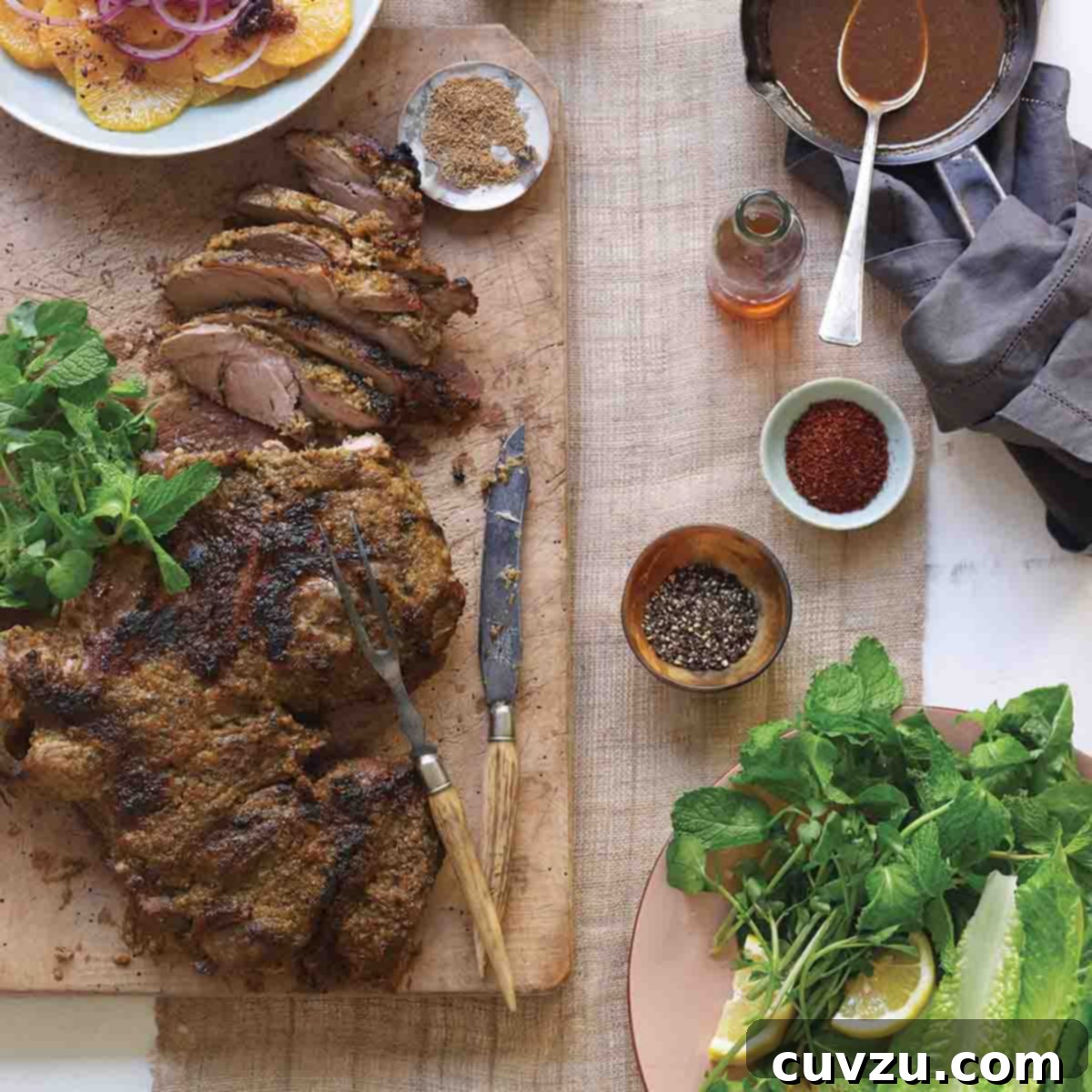 A partially carved roast leg of lamb on a wooden cutting board with spices, fresh herbs, and citrus salad surrounding it.