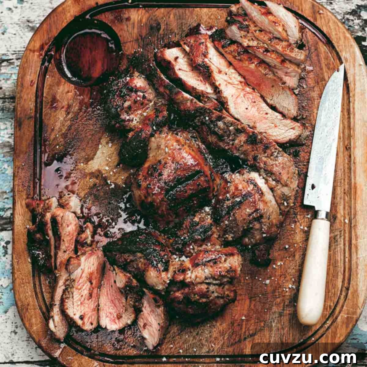 A carved butterflied grilled boneless leg of lamb on a wooden cutting board with a knife resting beside the meat.