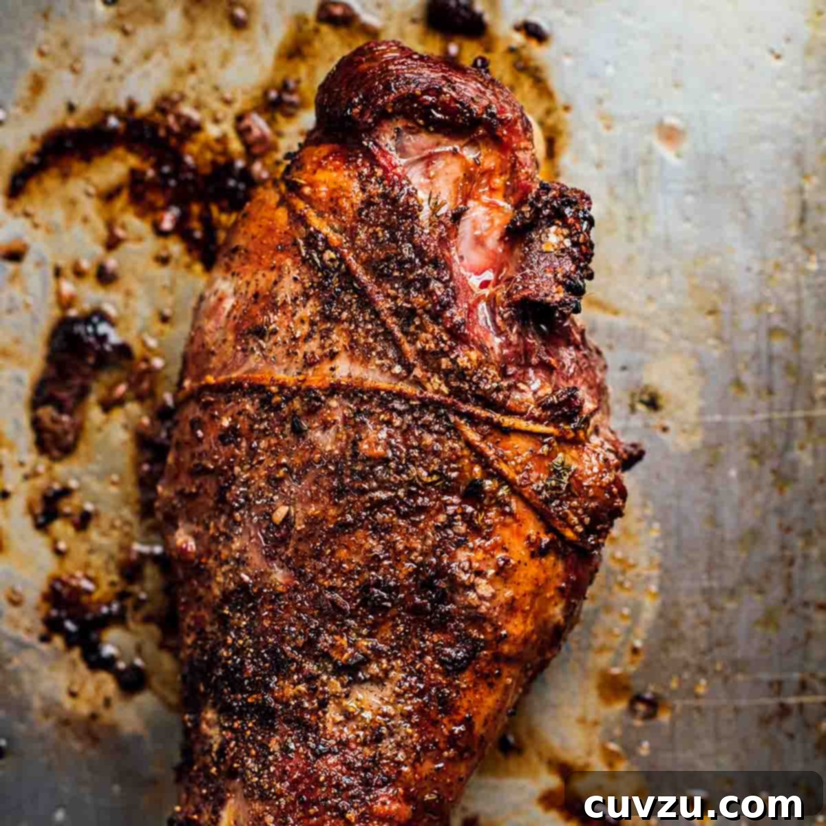 A whole roasted leg of lamb on a baking sheet with a garlic rub.