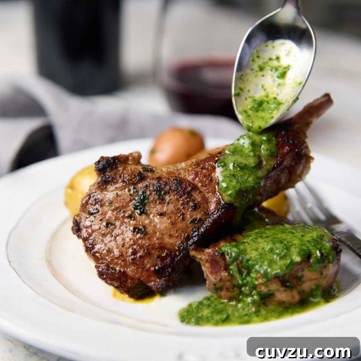 Juicy lamb chops on a white plate with a drizzle of vibrant mint and cilantro sauce.