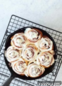 A cast-iron skillet filled with glazed biscuit cinnamon rolls on a wire rack.