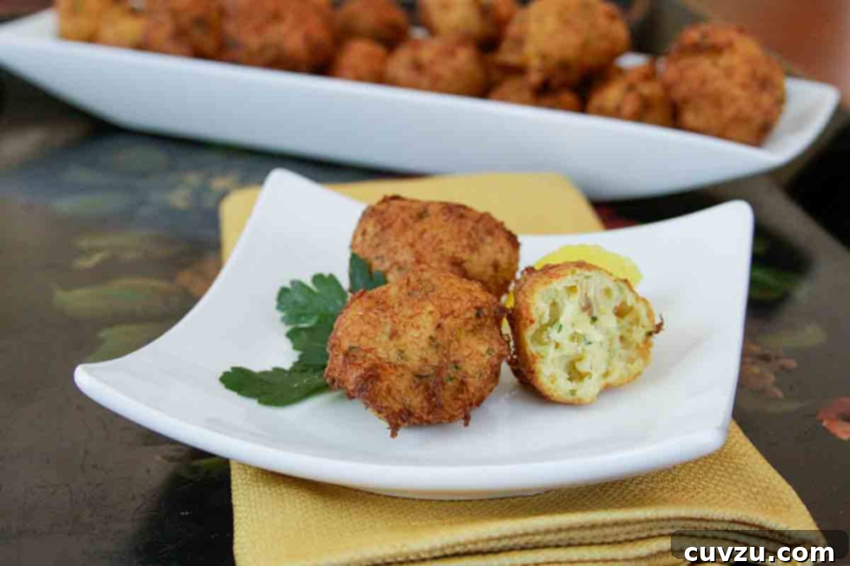 Spanish Golden Cod Fritters 3 A close-up of three rustic Spanish cod fritters, also known as buñuelos de bacalao, on a square white plate with a sprig of fresh parsley. The fritters showcase their characteristic irregular, crispy edges, hinting at their delicate crunch.