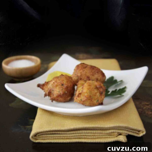 Three Spanish cod fritters, aka buñuelos de bacalao, on a square white plate with parsley on a yellow napkin and black tray