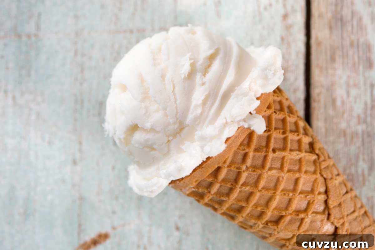 An ice cream cone with a scoop of toasted coconut ice cream on a white wood background.