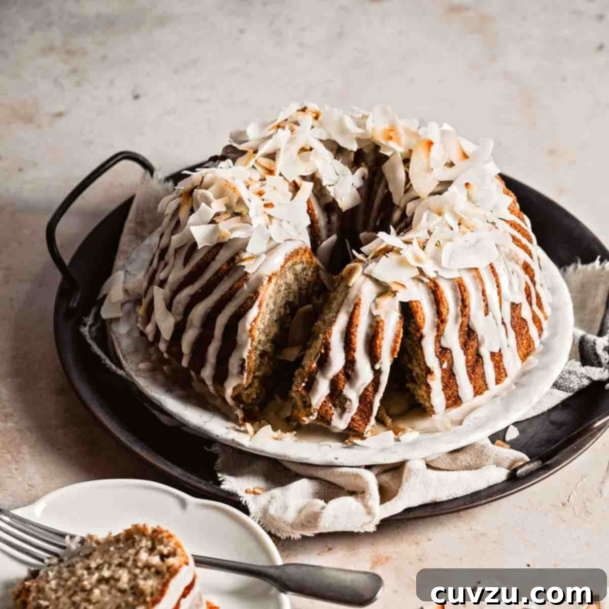 A banana coconut rum bundt cake on a metal try with a slice cut from in on a plate nearby.