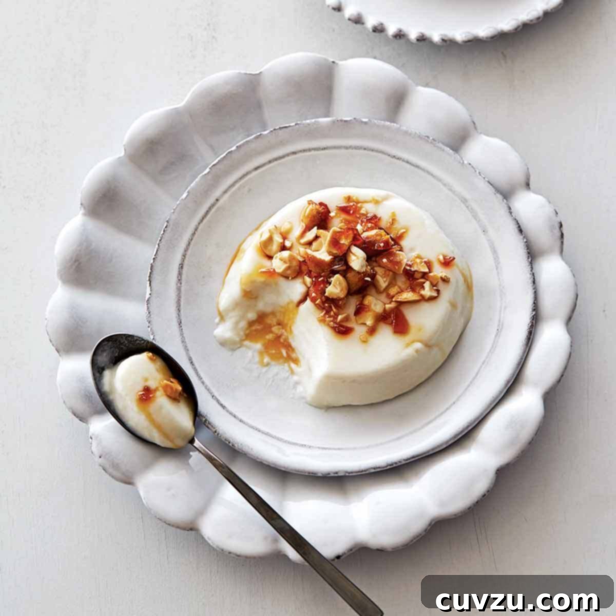A coconut panna cotta topped with peanut brittle crunch on a white plate.