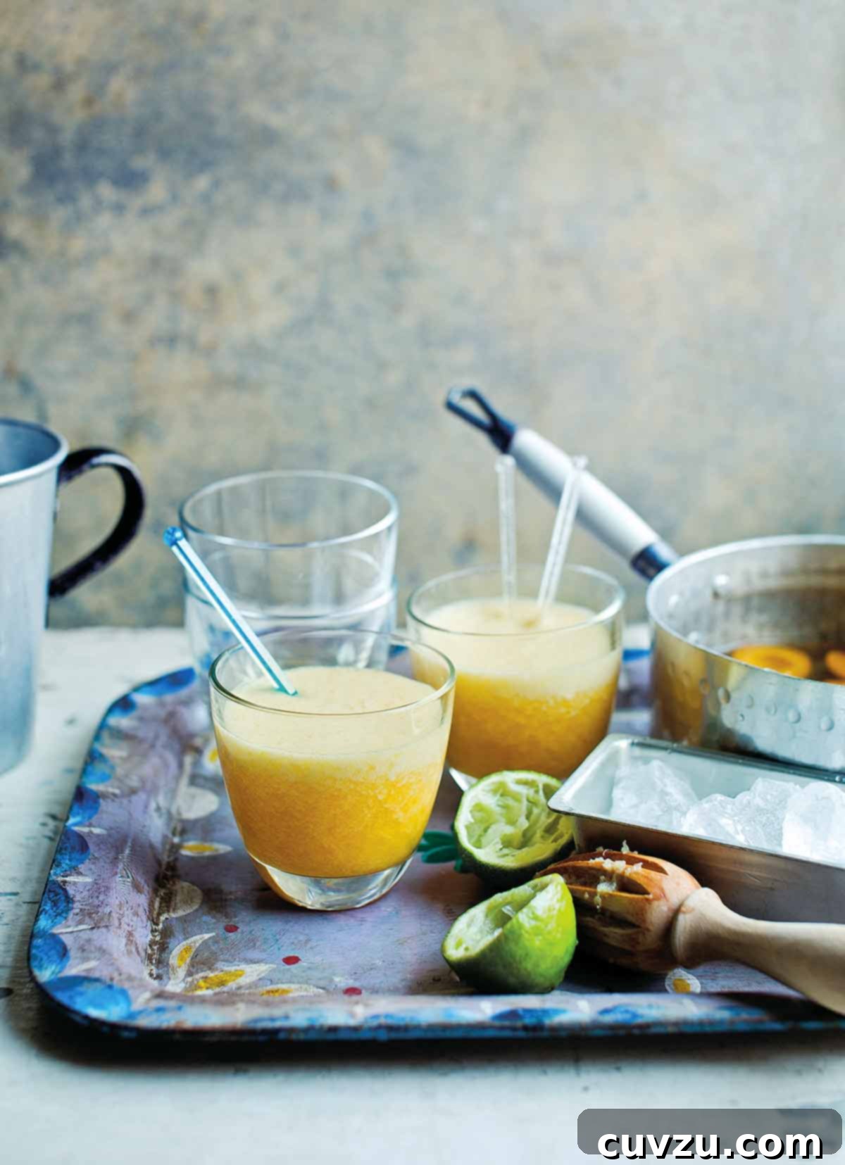 A metal serving tray with two apricot daiquiris with stir sticks, a juiced lemon, and a pot with poached apricots.
