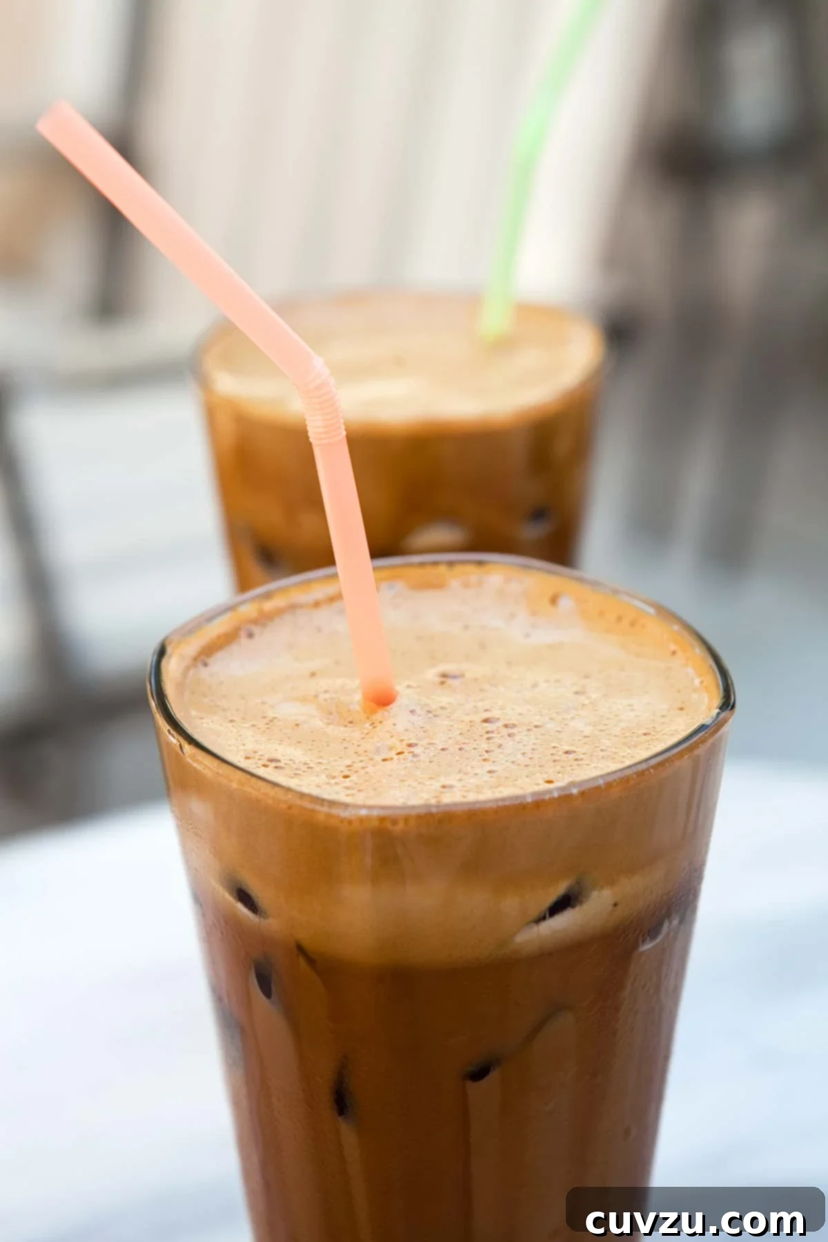 Two tall glasses filled with Greek-style frappe, with colorful straws standing up in them.