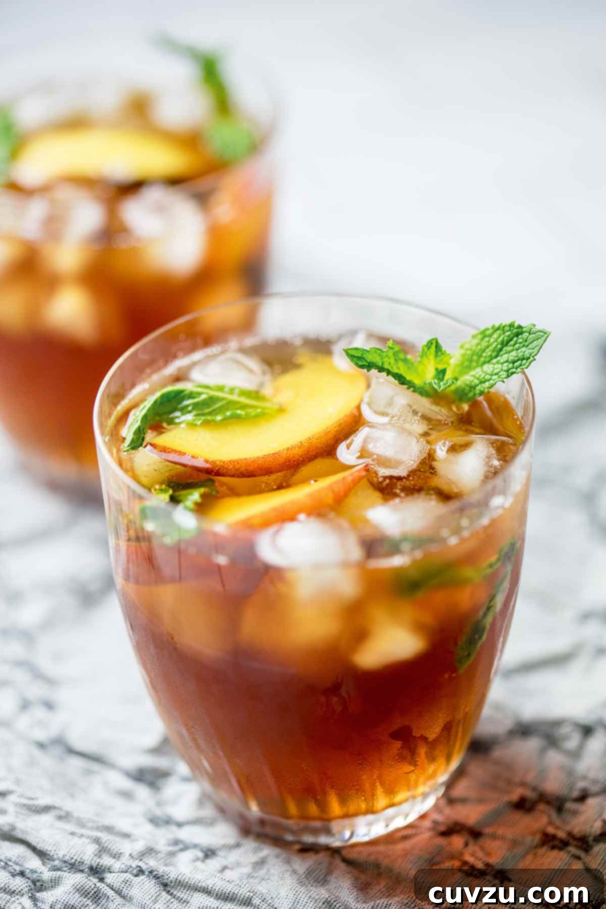 Two glasses of peach iced tea with mint leaves and peach slices for garnish.