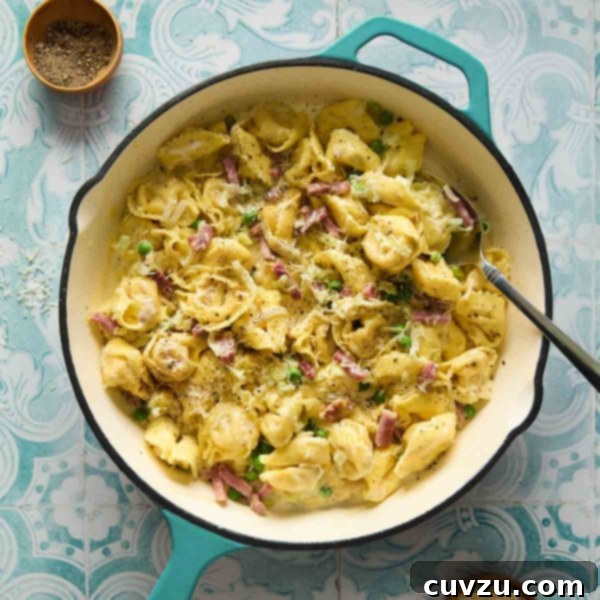 Creamy One-Pan Prosciutto Pea Tortellini 9 A deep skillet filled with tortellini with peas and prosciutto with bowls of pepper and cheese on the side.