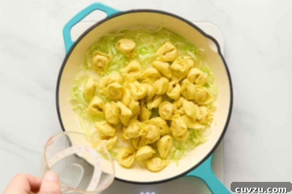 Creamy One-Pan Prosciutto Pea Tortellini 11 Tortellini and water being added to a skillet with leeks.