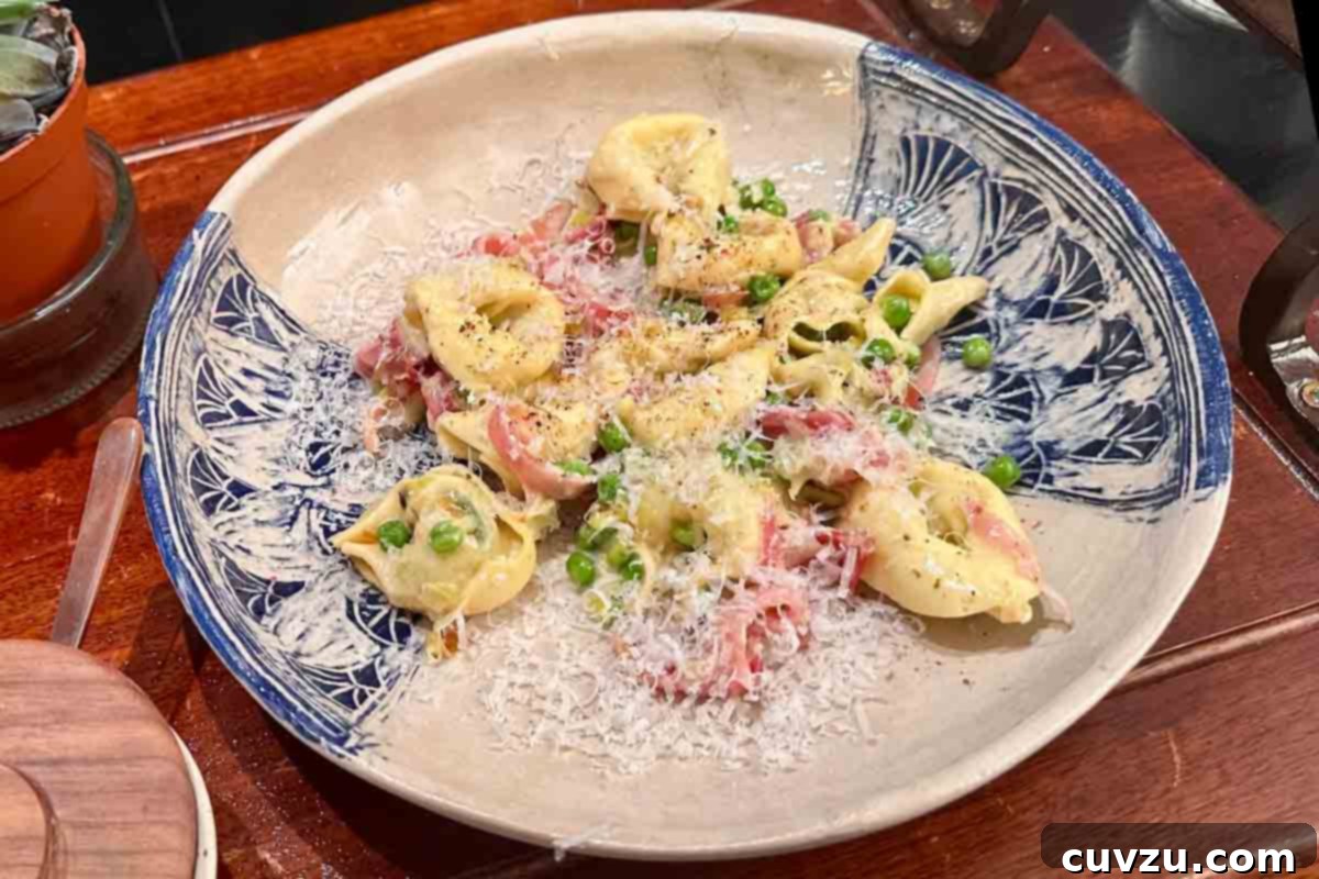 Creamy One-Pan Prosciutto Pea Tortellini 15 A shallow serving bowl filled with a generous portion of creamy tortellini with prosciutto and peas, elegantly topped with freshly grated Parmesan cheese.