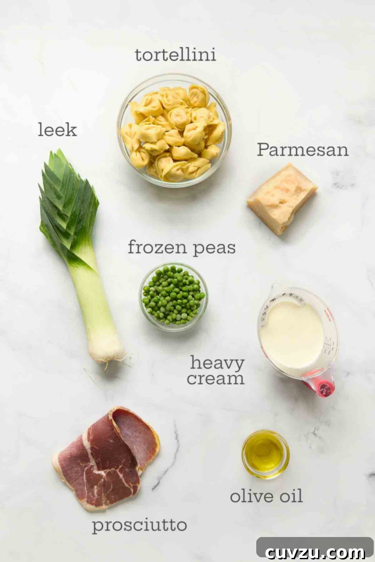 Creamy One-Pan Prosciutto Pea Tortellini 5 A vibrant display of ingredients for one-pot tortellini: fresh tortellini, a neatly sliced leek, a block of Parmesan cheese, a bag of frozen peas, a carton of heavy cream, a bottle of olive oil, and slices of savory prosciutto.