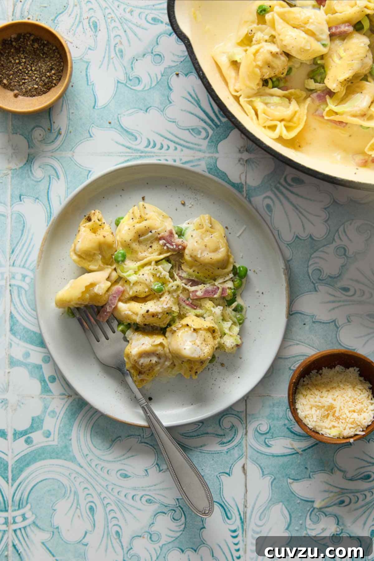 Creamy One-Pan Prosciutto Pea Tortellini 8 A generous serving of one-pot tortellini with prosciutto and peas on a white plate, with the remaining pasta still in the deep skillet nearby, ready for more servings.