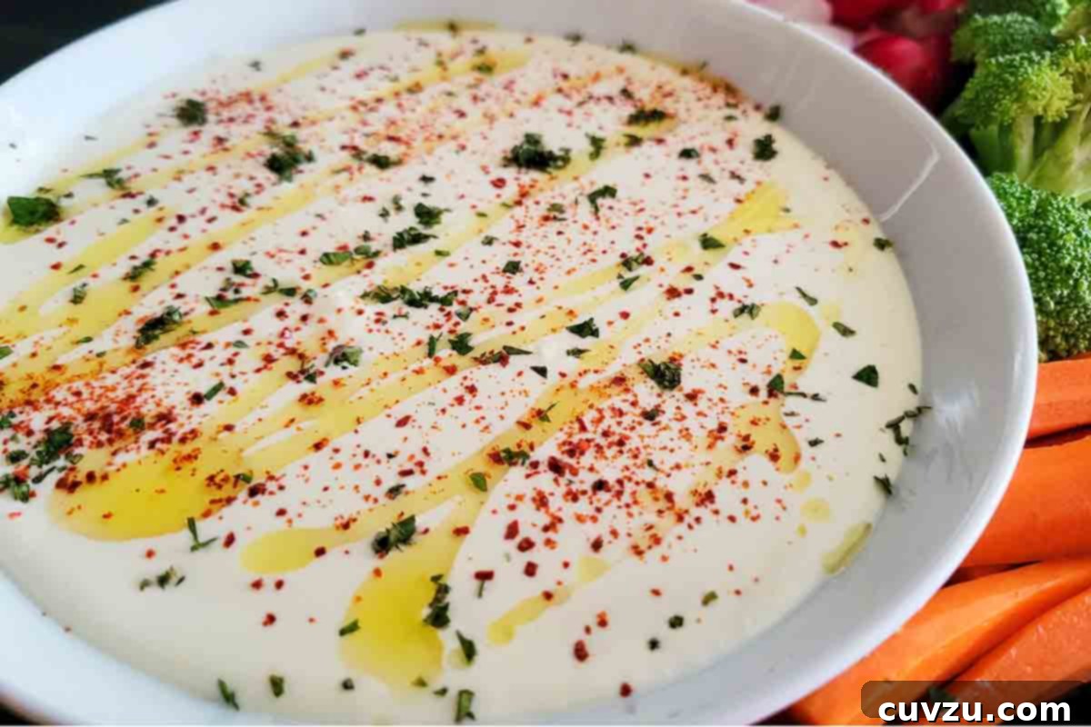 Creamy Whipped Feta 18 A white bowl filled with feta dip drizzled with oil and topped with spices, with raw veggies on the side.