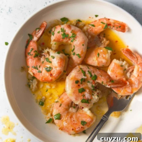 Garlic Lemon Shrimp Scampi 10 A wide shot of shrimp scampi in a white bowl, drenched in garlic butter sauce and garnished with parsley. A lemon wedge sits nearby, with scattered herbs and sauce on the table.