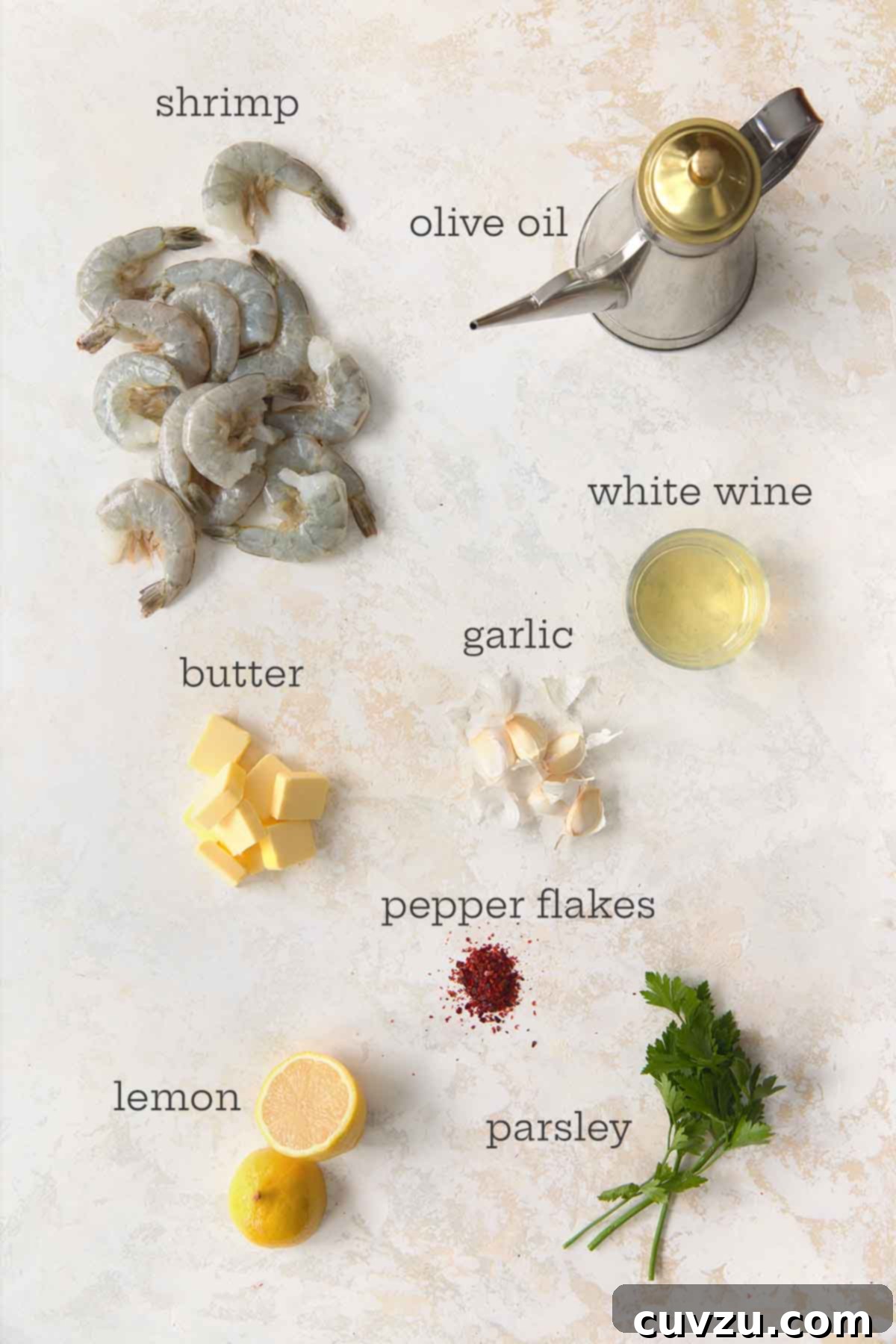 Garlic Lemon Shrimp Scampi 5 Overhead view of raw shrimp, olive oil, white wine, garlic cloves, butter cubes, red pepper flakes, lemon halves, and fresh parsley arranged on a light surface.