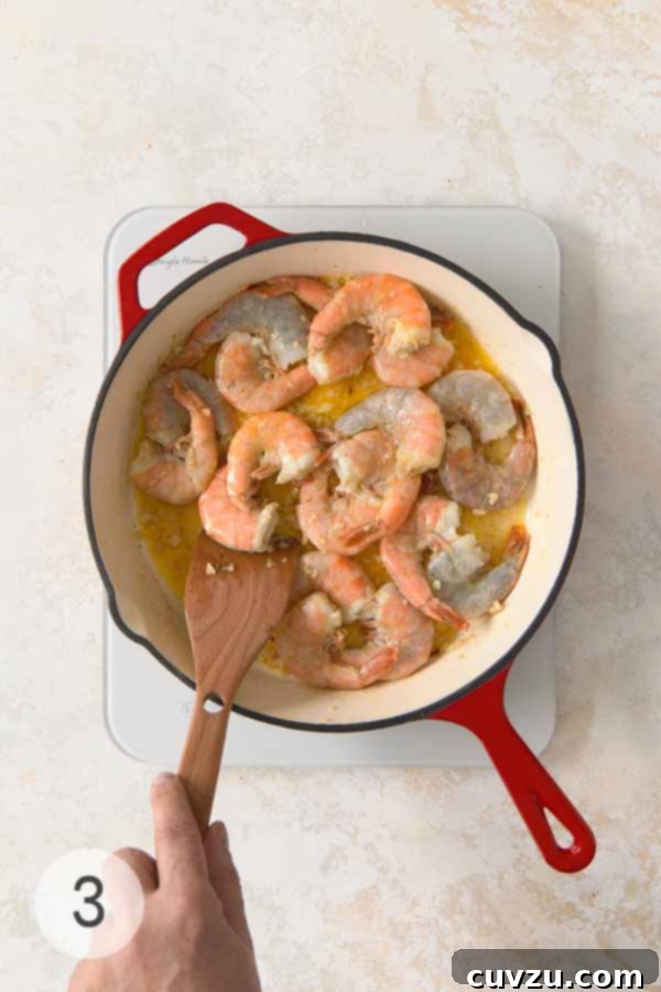 Garlic Lemon Shrimp Scampi 8 Raw shrimp cooking in a garlic butter and white wine sauce in a skillet, stirred with a wooden spatula.