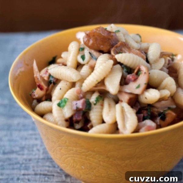 Pancetta and Chanterelle Gnocchetti with Fresh Mint 3 A close-up shot of a bowl of gnocchetti pasta, featuring savory ham, golden chanterelle mushrooms, and fresh mint leaves, ready for serving.