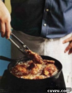 Classic Southern Skillet Fry 3 A chef holds tongs, presenting freshly pan-fried Southern chicken, golden and crispy, above a simmering skillet