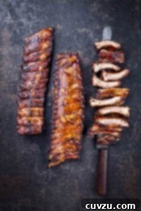 Two racks of barbecued baby back ribs, and a third rack cut into individual ribs, resting on a knife.