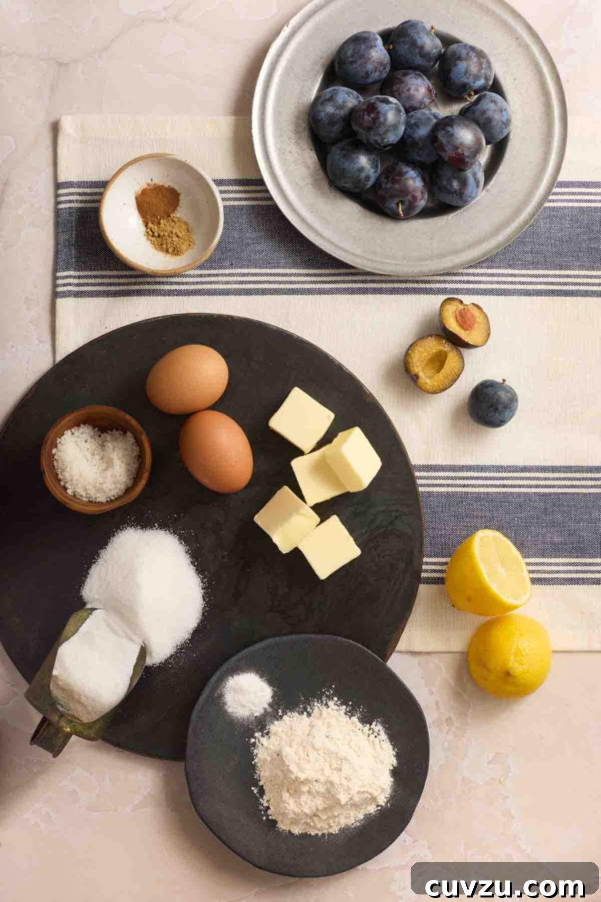 Golden Plum Torte 5 A collection of essential ingredients for plum torte: flour, sugar, butter, eggs, fresh lemons, and vibrant fresh plums, arranged artfully on a countertop.