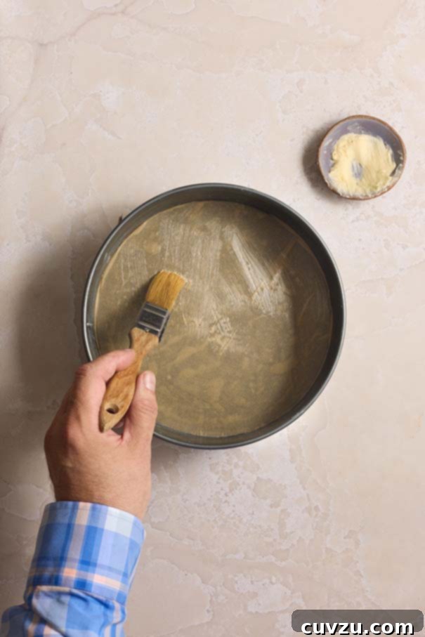 Golden Plum Torte 6 A hand expertly uses a pastry brush to generously grease a springform pan with softened butter, preparing it for the torte batter.