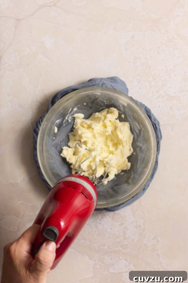 Golden Plum Torte 7 Creaming together butter and granulated sugar in a clear glass mixing bowl, illuminated by a red hand mixer, creating a light and fluffy mixture.