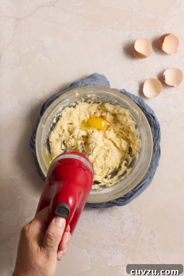 Golden Plum Torte 9 A single egg being gently cracked into the creamy plum torte batter in a glass mixing bowl, illustrating the process of incorporating eggs one at a time.