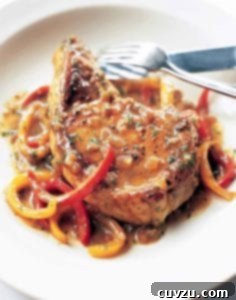 A close-up of a perfectly seared pork chop with a medley of sweet peppers and sauce.