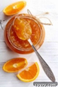 A jar of orange marmalade with a spoon resting on top and a few orange wedges beside it.