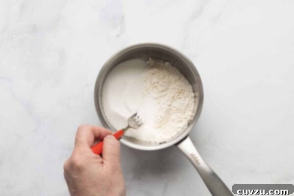 Tropical Coconut Dream Pie 14 A man's hand stirring flour, salt, and sugar in a saucepan.