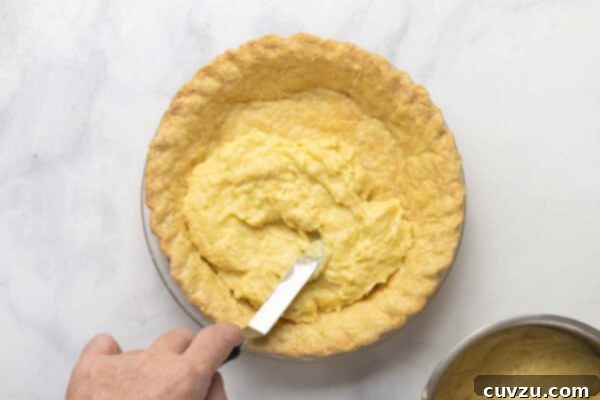 Tropical Coconut Dream Pie 19 A man's hand spreading coconut custard into a baked pie shell.