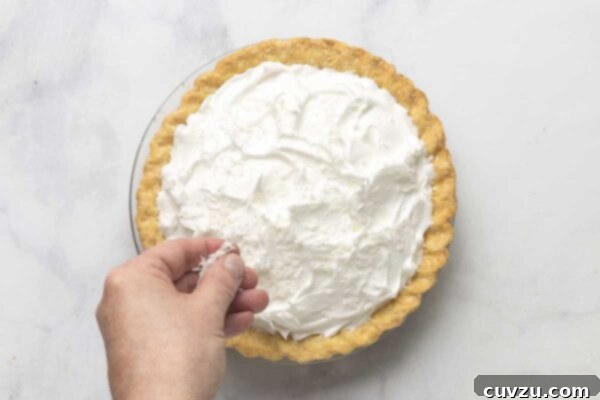 Tropical Coconut Dream Pie 23 A coconut cream pie being sprinkled with shredded coconut.