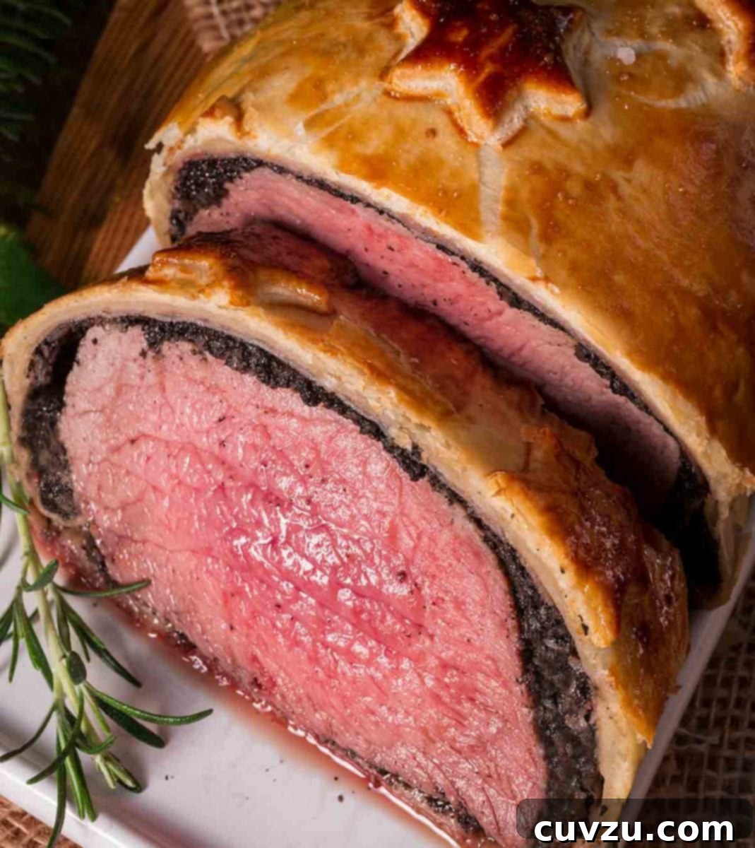 Filet Mignon in Golden Crust 2 Close-up of a golden-baked Beef Wellington on a white plate, garnished with a sprig of fresh rosemary, showcasing its flaky pastry and perfect crust.