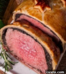 Close-up of a golden-baked Beef Wellington on a white plate, garnished with a sprig of fresh rosemary.