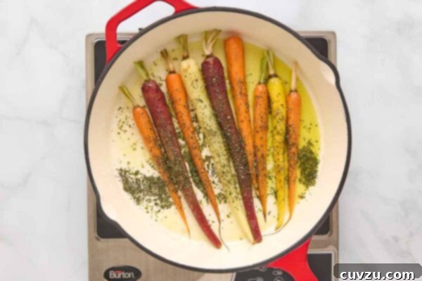 Carrots in a skillet with fresh rosemary being stirred, releasing their aromatic oils.