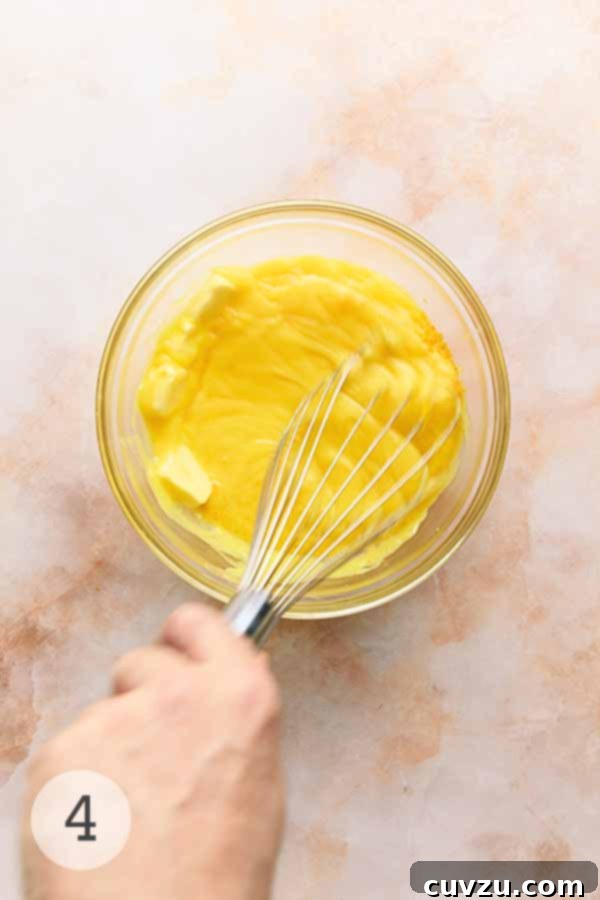 Meyer Lemon Curd: Zesty Citrus Delight 8 A man's hand whisking Meyer lemon curd, lemon zest, and butter together in a bowl until smooth and emulsified.