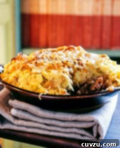 A porcelain bowl filled with shepherd's pie and topped with potatoes, onions, and cheddar, showcasing its delicious layers.